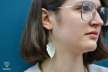 Charger l&#39;image dans la galerie, Jeune femme portant des boucles d&#39;oreilles argentées en origami blanches et argentées en forme de feuille
